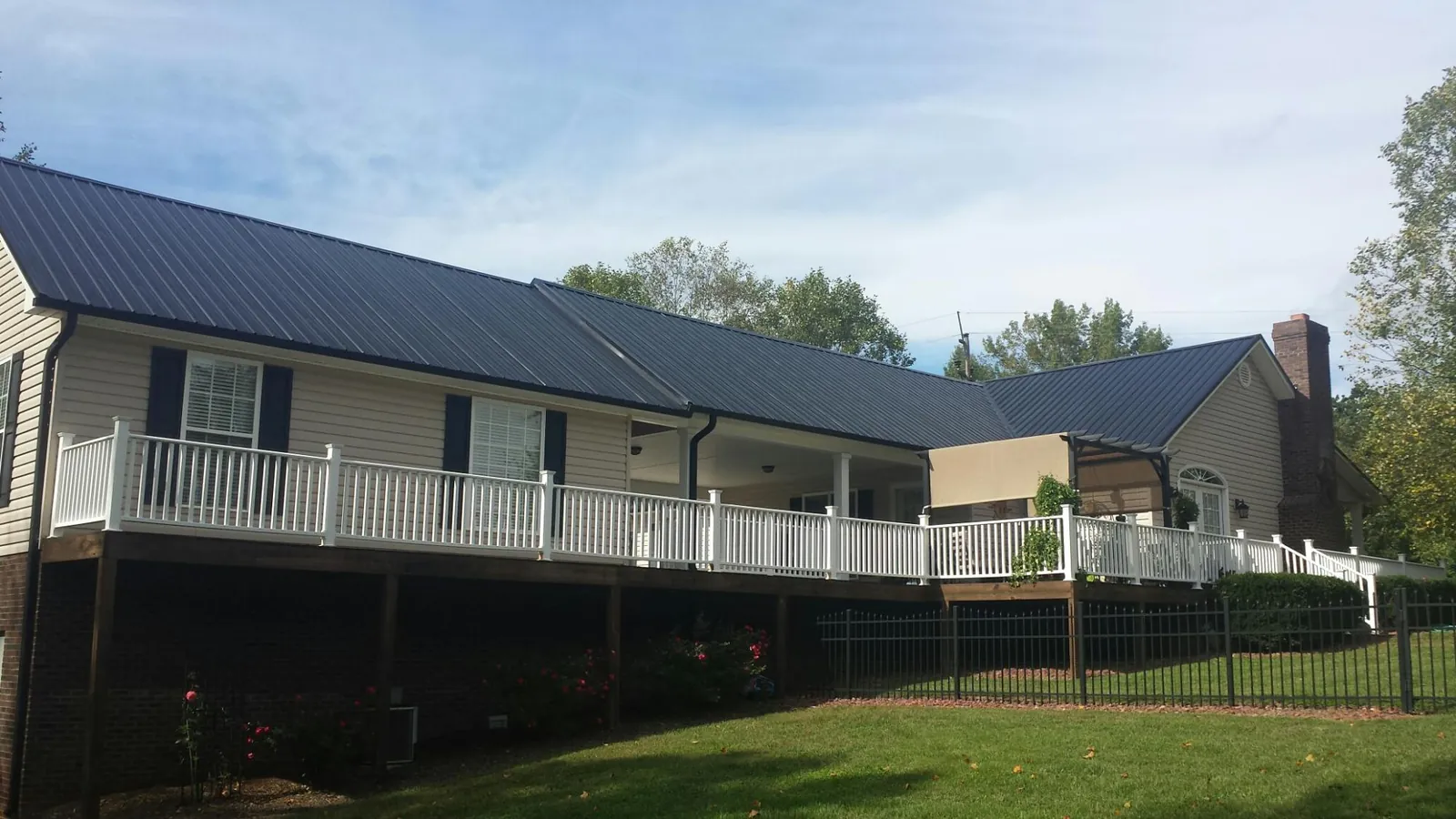 Black metal roof above a long white railed deck on a hillside home in Hugo