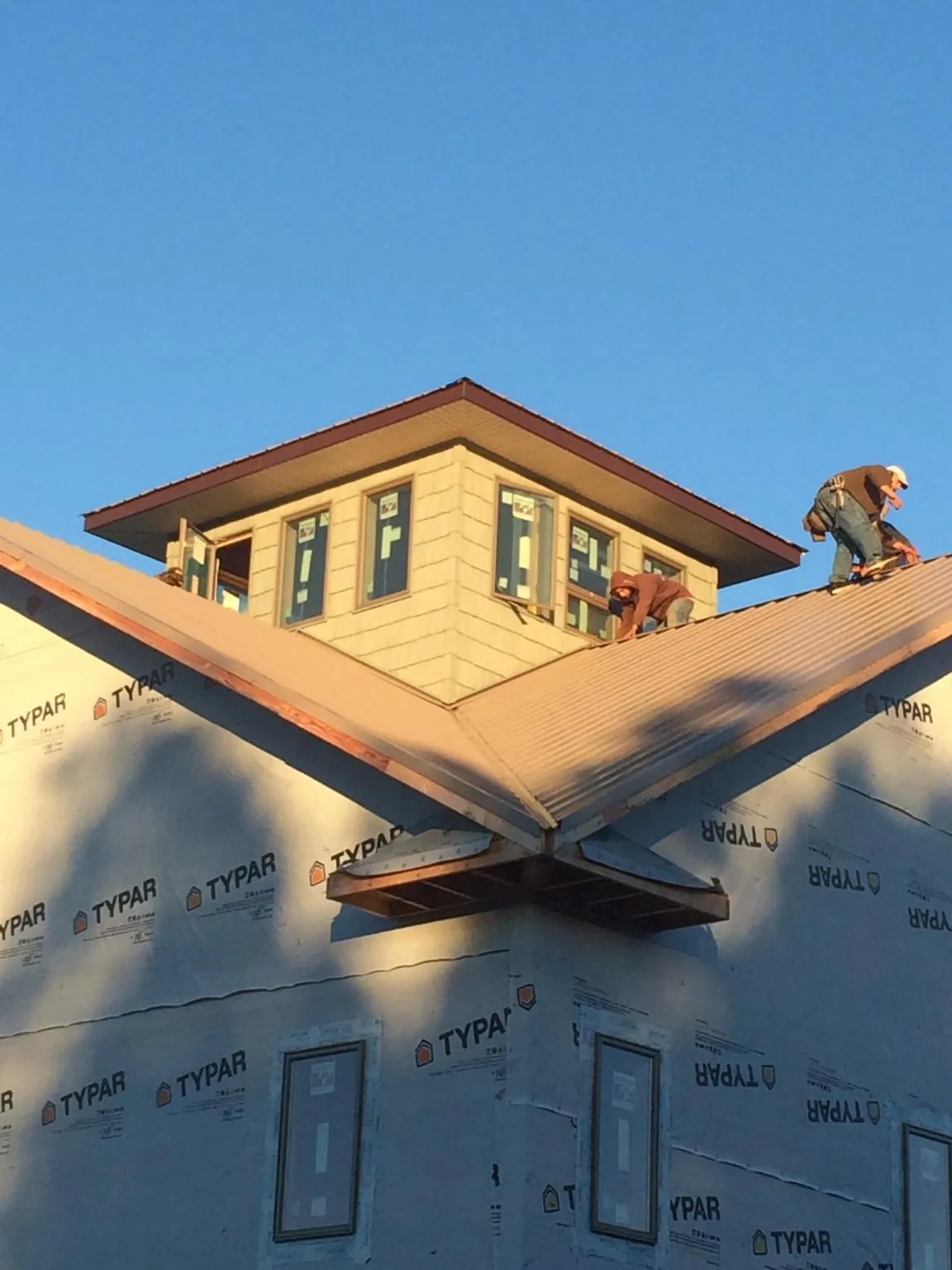 Roofers working around a rooftop cupola on a new metal roof at sunset — Roof Waterproofing in Hugo by Roofing Brothers